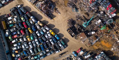 צילום אוויר של מגרש פירוק רכבים המלא במאות מכוניות שחונות בשורות צפופות לצד ערימות גרוטאות וכלים כבדים.