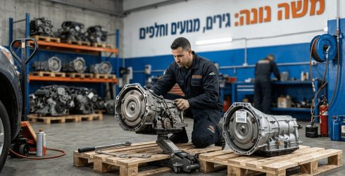 תמונה מפורטת של מוסך חלקי חילוף לרכב מציגה מכונאי כורע על רצפת הבטון ובודק מכלול גיר אוטומטי המונח על משטח עץ עם מפתח ברגים לצידו כאשר מכלול גיר מפירוק נוסף עומד לידו וברקע נראים מדפי אחסון עמוסים במנועים נוספים ושלט גדול בעברית על הקיר המכריז משה נונה גירים מנועים וחלפים